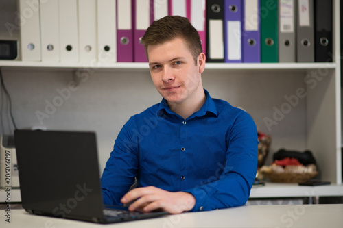 Portrait of a handsome young male manager in an office sitting at a table with a laptop.