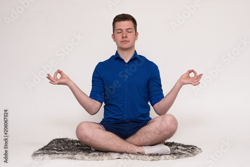 Portrait of a young handsome man on a white background sitting on the floor in a pose of Zen photo