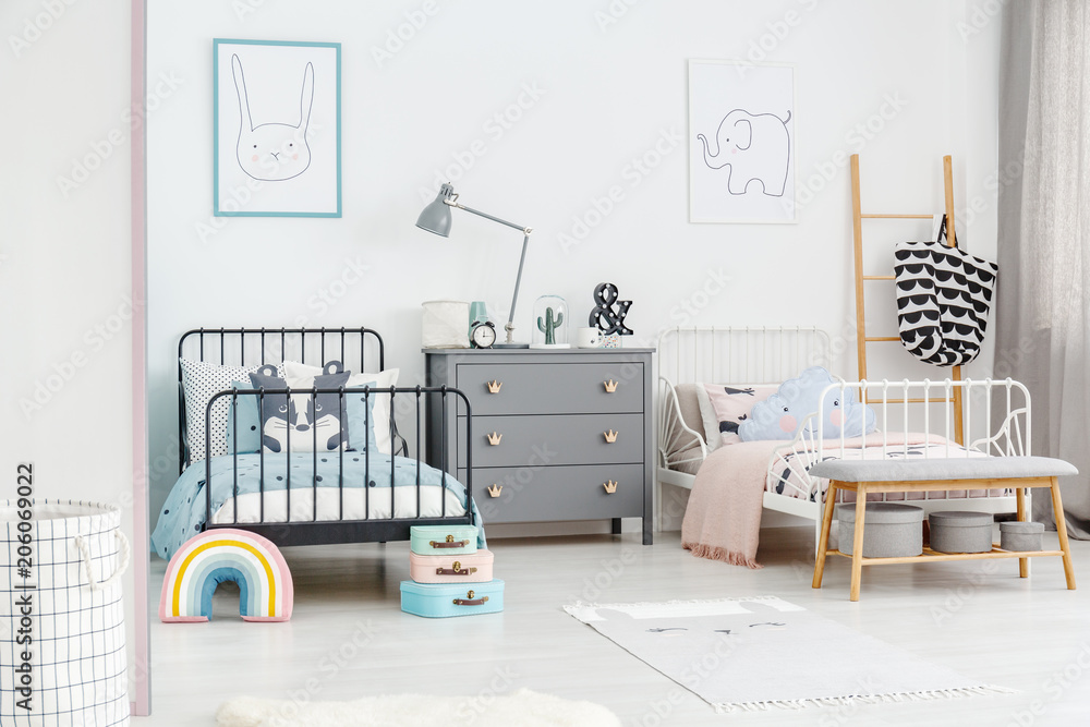 Fototapeta premium Lamp on grey cabinet between black and white bed in siblings bedroom interior with posters. Real photo