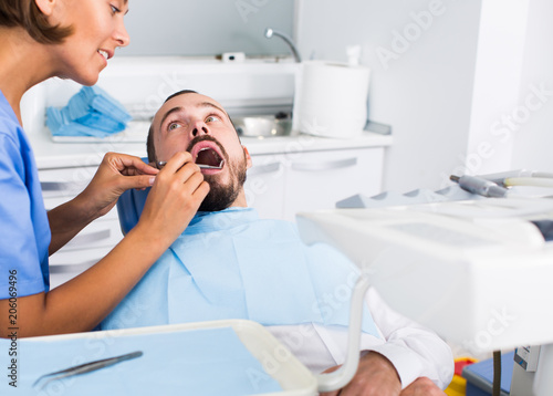 doctor woman in uniform is examinating of man on the chair in the dental office