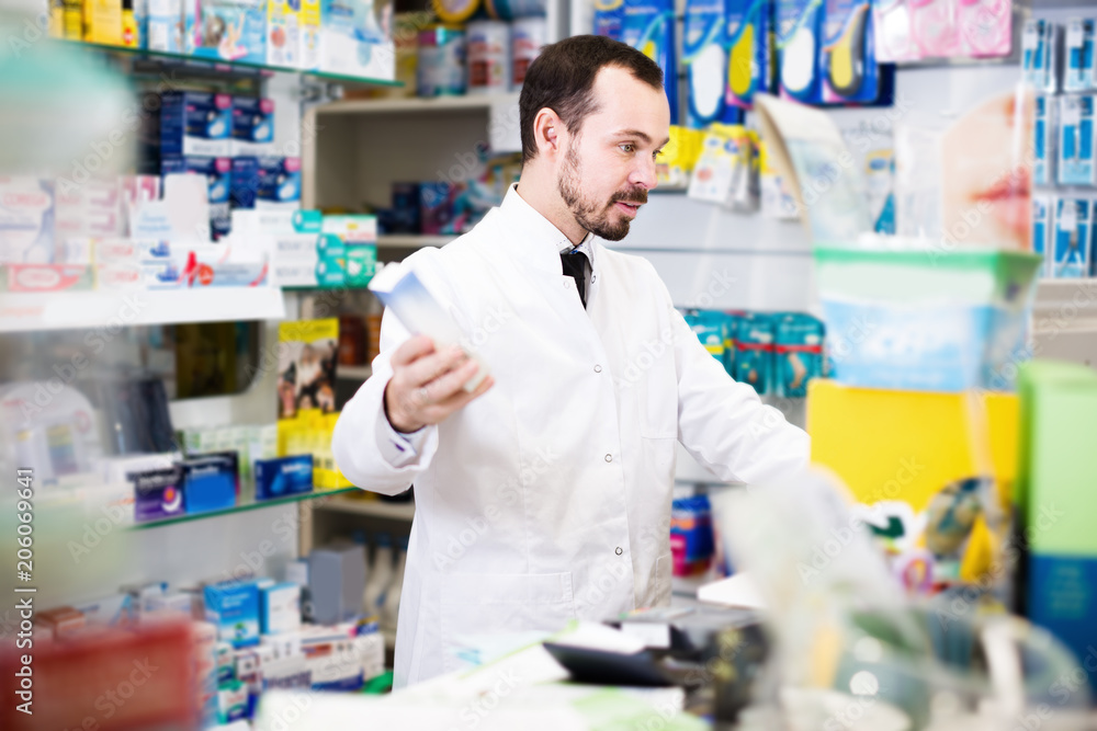 Smiling man pharmacist looking rows of drugs