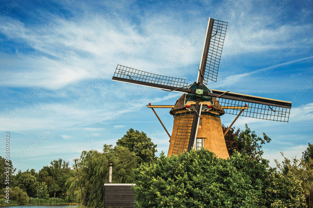 Wooden windmill, leafy bushes and sunny blue sky at Weesp. Quiet and pleasant village full of canals and green near Amsterdam. Northern Netherlands.