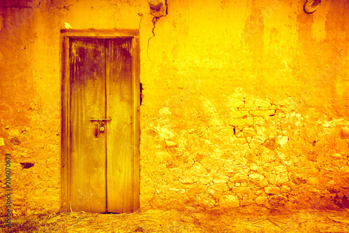 Stylish cracked vintage bright wall in yellow orange shades with royal blue wooden door. Ideal background for retro style illustrations and collages. Grunge style. Artistic retouching.