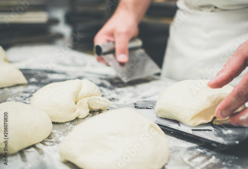 Hands of a male baker measuring pieces of wheat dough for bread or pizza