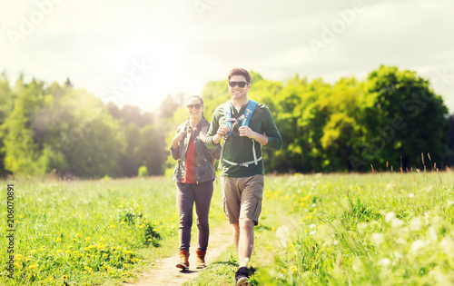 travel, hiking, backpacking, tourism and people concept - happy couple with backpacks and walking along country road outdoors