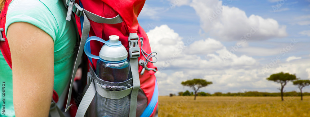 travel, tourism, hike and people concept - close up of woman with water bottle in backpack pocket over african savannah background - obrazy, fototapety, plakaty 