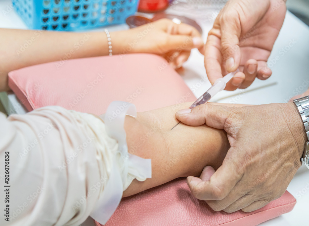 Nurse injecting with syringe to patient's arm drawing blood sample for blood test in hospital Nurse injecting with syringe to patient's arm drawing blood sample for blood test in hospital