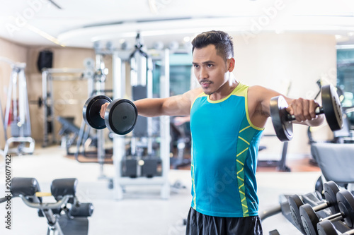 Portrait of a handsome determined young man exercising with dumbbells during upper-body workout routine in a modern fitness club