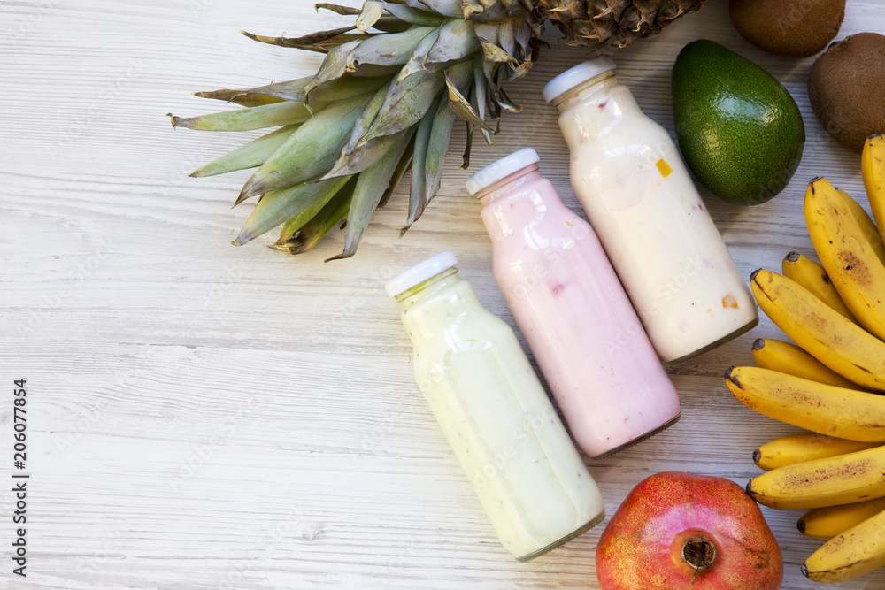 Fruit smoothies of different tastes in glass jars with ingredients on white wooden background. Top view, from above. Flat lay. Copy space.