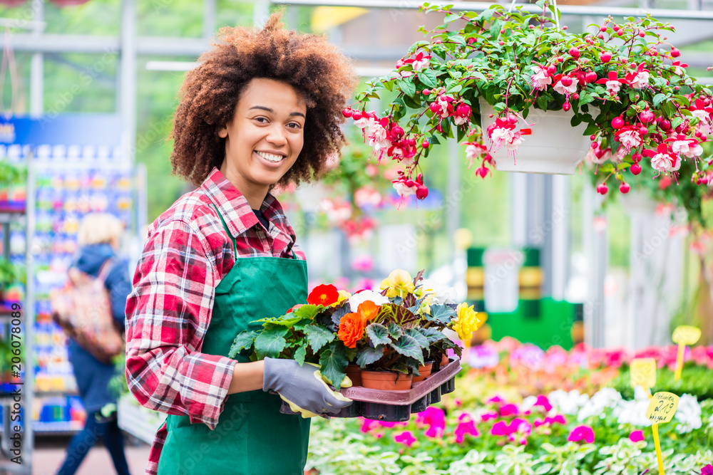 Portrait of a cheerful young woman wearing green apron and gardening gloves while working with dedication as florist in a modern flower shop