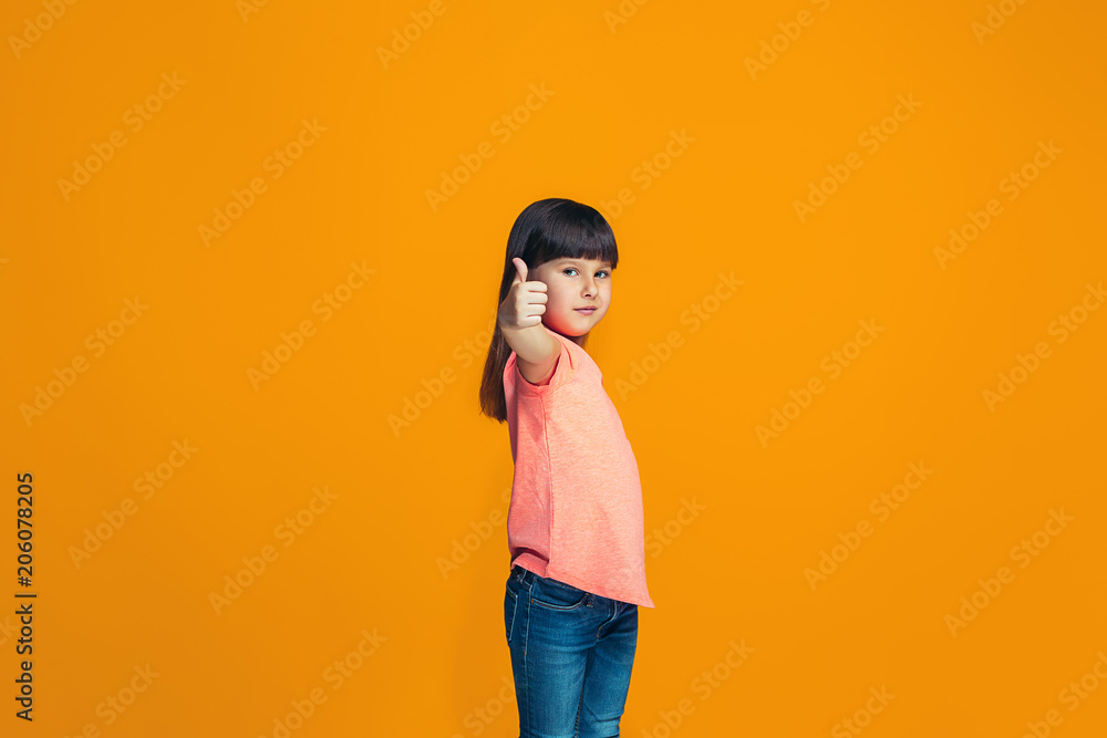The happy teen girl standing and smiling against orange background. The happy teen girl standing and smiling against orange background.