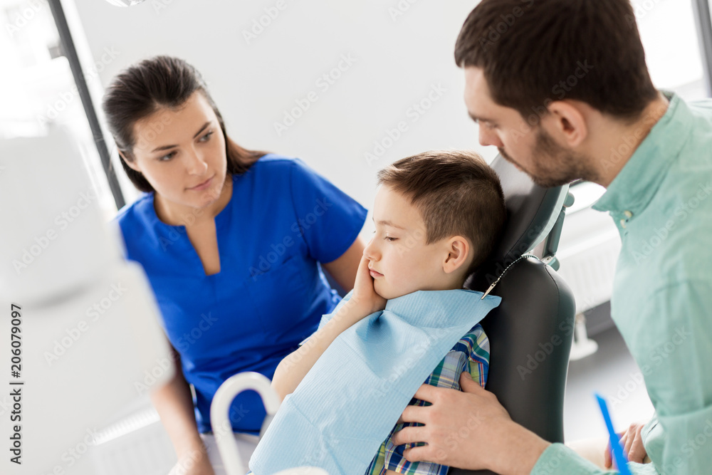 Fototapeta premium medicine, dentistry and healthcare concept - father and son suffering from toothache visiting dentist at dental clinic