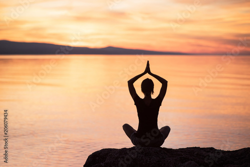 Silhouette of a young woman doing yoga near the sea at sunset. Harmony, meditation and healthy lifestyle concept