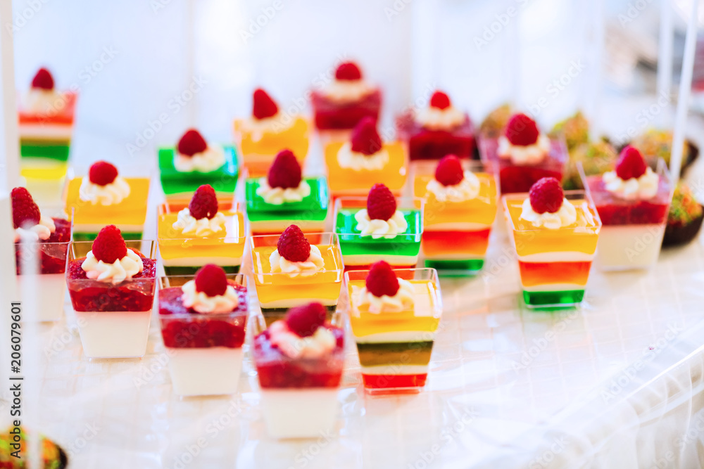 Close-up of a colored jelly with cream and raspberry in transparent cups on a table with a white cloth