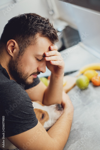 Man hugging his dog while having headache in the kitchen