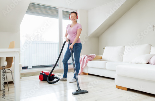 household, housework and music concept - happy woman or housewife with vacuum cleaner and headphones cleaning floor at home