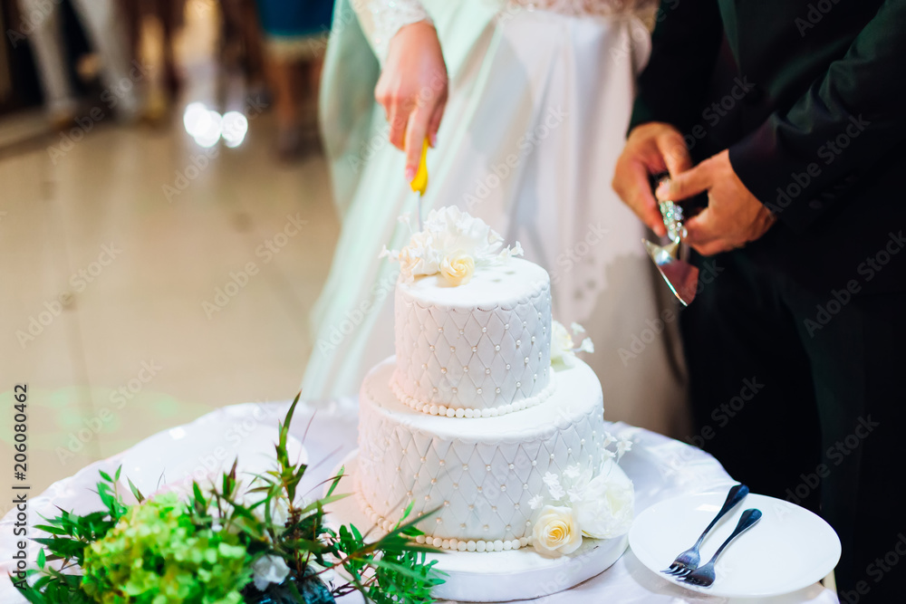 multilevel wedding cake on a round table. Newlyweds are standing next to one and cutting a wedding cake multilevel wedding cake on a round table. Newlyweds are standing next to one and cutting a wedding cake