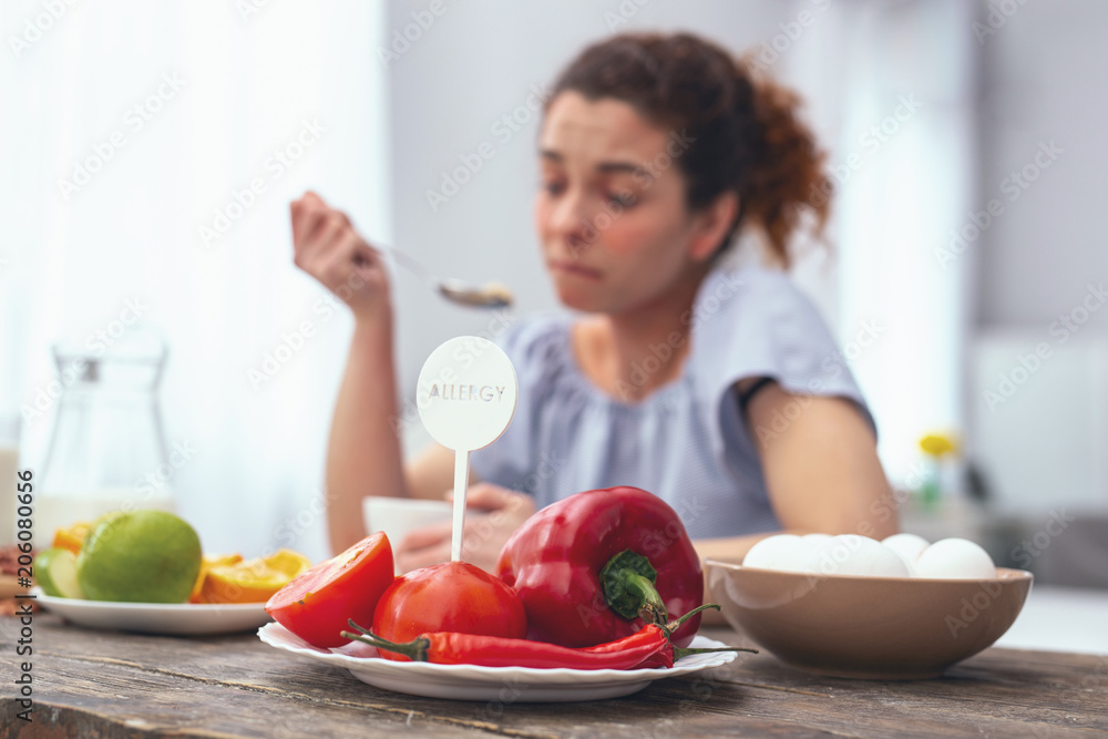 Vegetable allergens. Young lady at a kitchen table eating her meal while avoiding touching and consuming allergy provoking vegetables Vegetable allergens. Young lady at a kitchen table eating her meal while avoiding touching and consuming allergy provoking vegetables