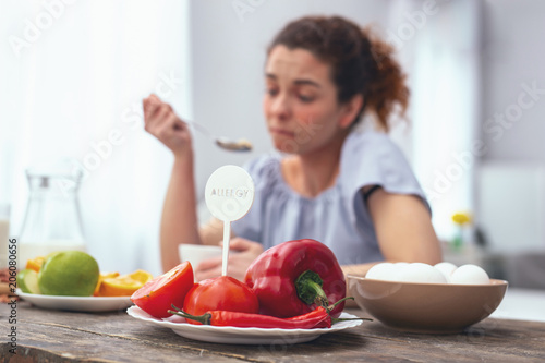 Vegetable allergens. Young lady at a kitchen table eating her meal while avoiding touching and consuming allergy provoking vegetables