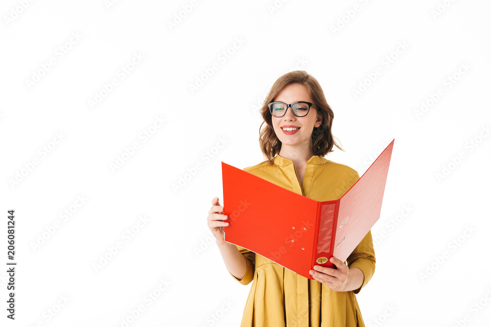 Portrait of young joyful lady in eyeglasses standing and happily looking in open red folder on white background isolated Portrait of young joyful lady in eyeglasses standing and happily looking in open red folder on white background isolated