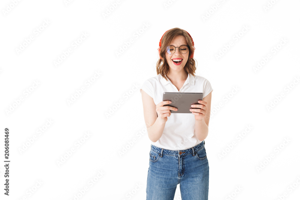 Portrait of young joyful lady in eyeglasses and headphones standing with the tablet in hands on white background isolated Portrait of young joyful lady in eyeglasses and headphones standing with the tablet in hands on white background isolated
