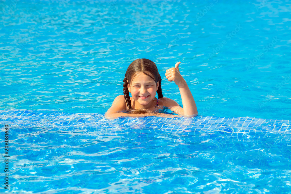 Kid swims in the pool and shows thumb up symbol.