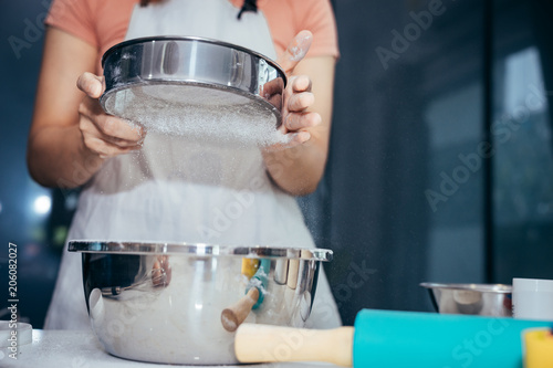 A woman sifting flour into a stainless bowl. Girl is sifting flour to making the bakery in her kitchen on weekend.