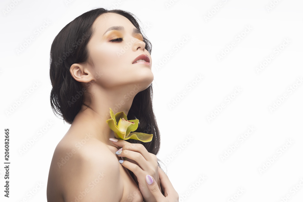 A beautiful brunette nude shoulders girl sensually holds a flower of an orchid in her hands. Nude make-up. Healthy smooth skin A beautiful brunette nude shoulders girl sensually holds a flower of an orchid in her hands. Nude make-up. Healthy smooth skin
