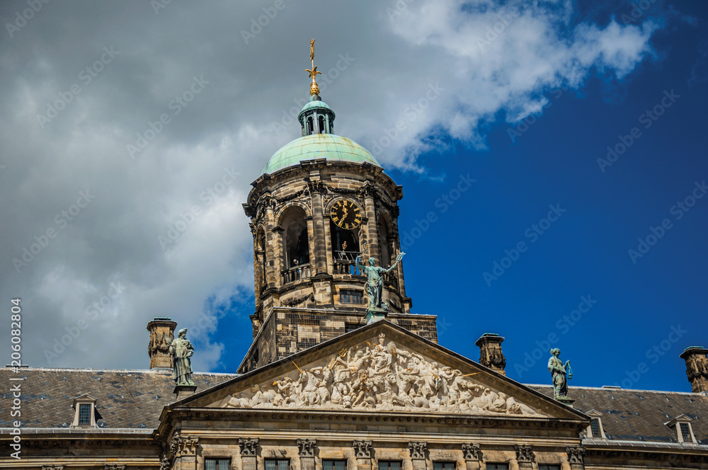 Close-up of facade with sculptures and dome with golden clock in the Royal Palace of Amsterdam. The city is famous for its huge cultural activity, graceful canals and bridges. Northern Netherlands.
