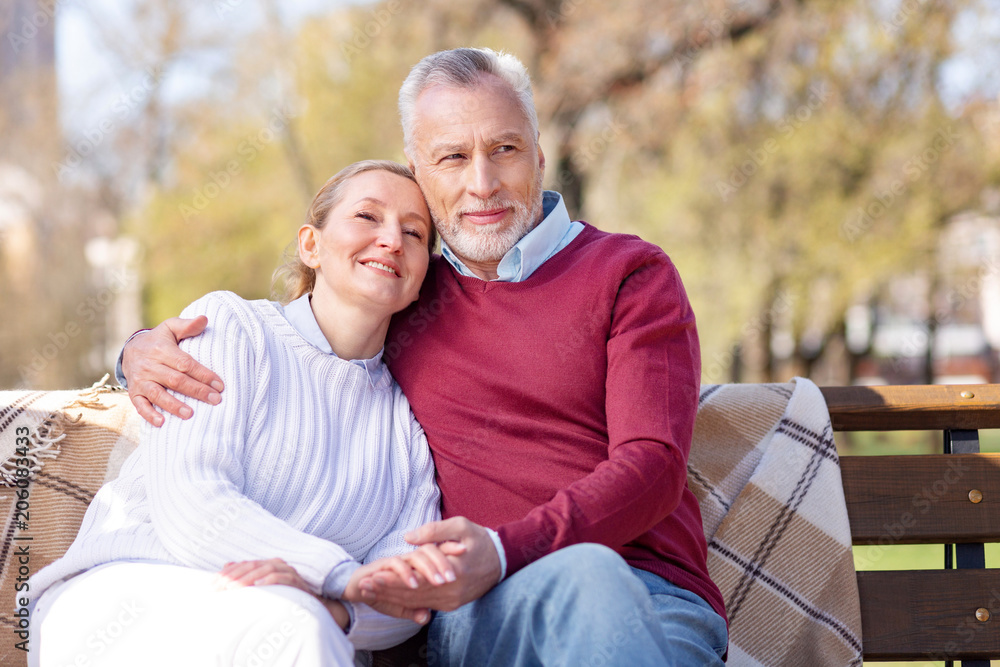 Fototapeta premium In the park. Positive aged couple resting on the bench while enjoying their weekend together
