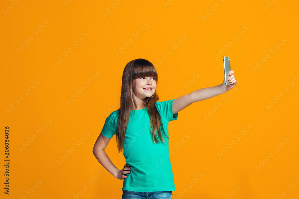 The happy teen girl standing and smiling against orange background. The happy teen girl standing and smiling against orange background.