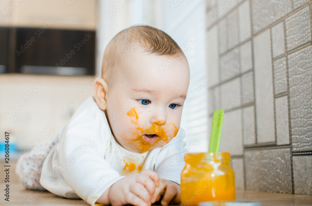 beautiful baby chest all dirty in fruit puree, pumpkin with spoon in hand next to a jar of food beautiful baby chest all dirty in fruit puree, pumpkin with spoon in hand next to a jar of food