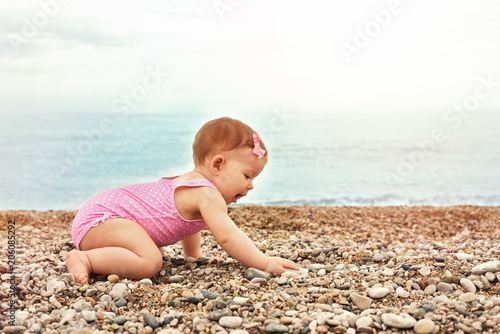 little girl in a pink swimsuit playing near the blue sea on a pebble beach