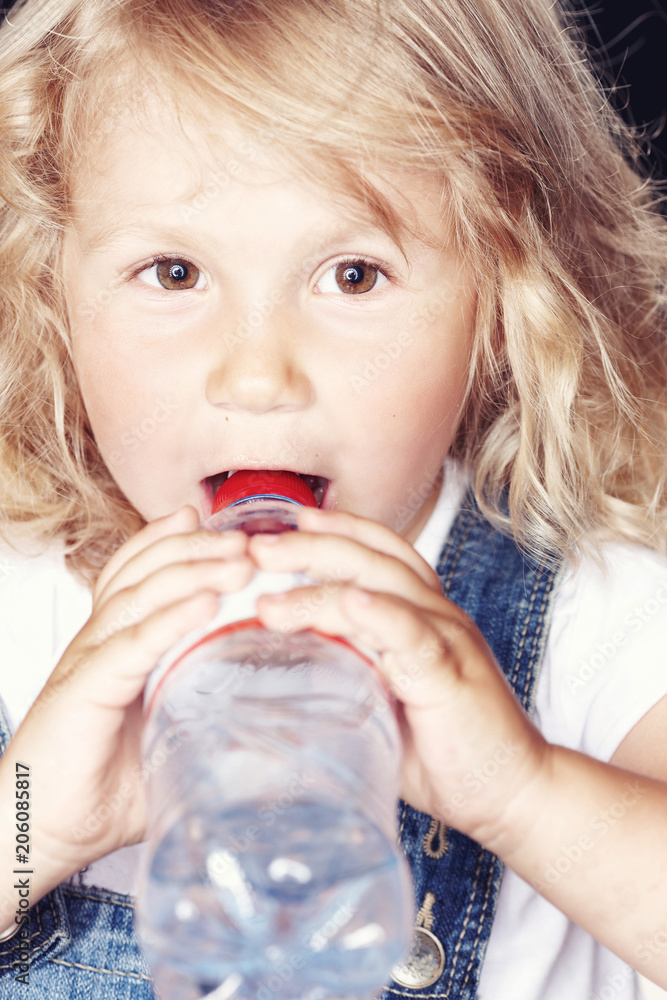 Portrait of a cute little girl in denim overalls, drink water while sitting in studio. Portrait of a cute little girl in denim overalls, drink water while sitting in studio.
