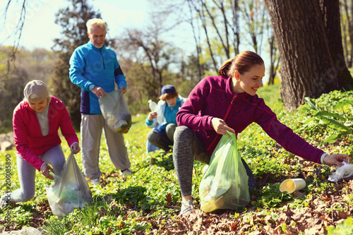 We are volunteers. Beautiful cheerful woman gathering litter while other volunteers helping her