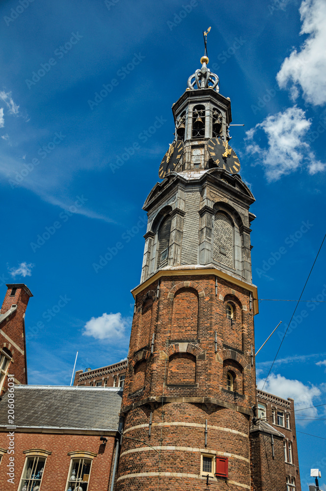 Close-up of pointed steeple roof in a brick building with golden clock and blue sky in Amsterdam. The city is famous for its huge cultural activity, graceful canals and bridges. Northern Netherlands.