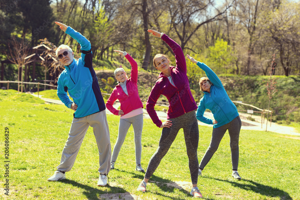 Fototapeta premium We love sport. Pretty alert woman smiling and training aged people in the open air