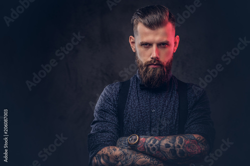Fotografía Portrait of a handsome old-fashioned hipster in a blue shirt and suspenders, standing with crossed arms in a studio