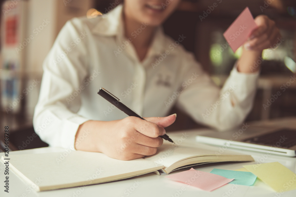 Close up and front view Cropped view of woman hand writing in notebook and sitting at table with laptop. Copy space concept Close up and front view Cropped view of woman hand writing in notebook and sitting at table with laptop. Copy space concept