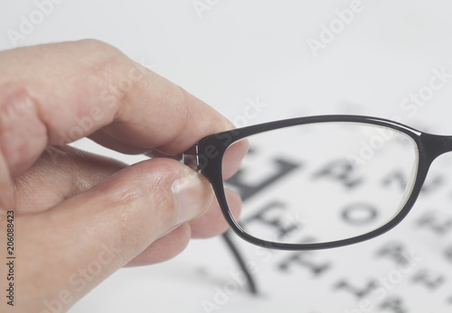 Male hand holding black Eyeglasses for vision eyesight examination test chart
