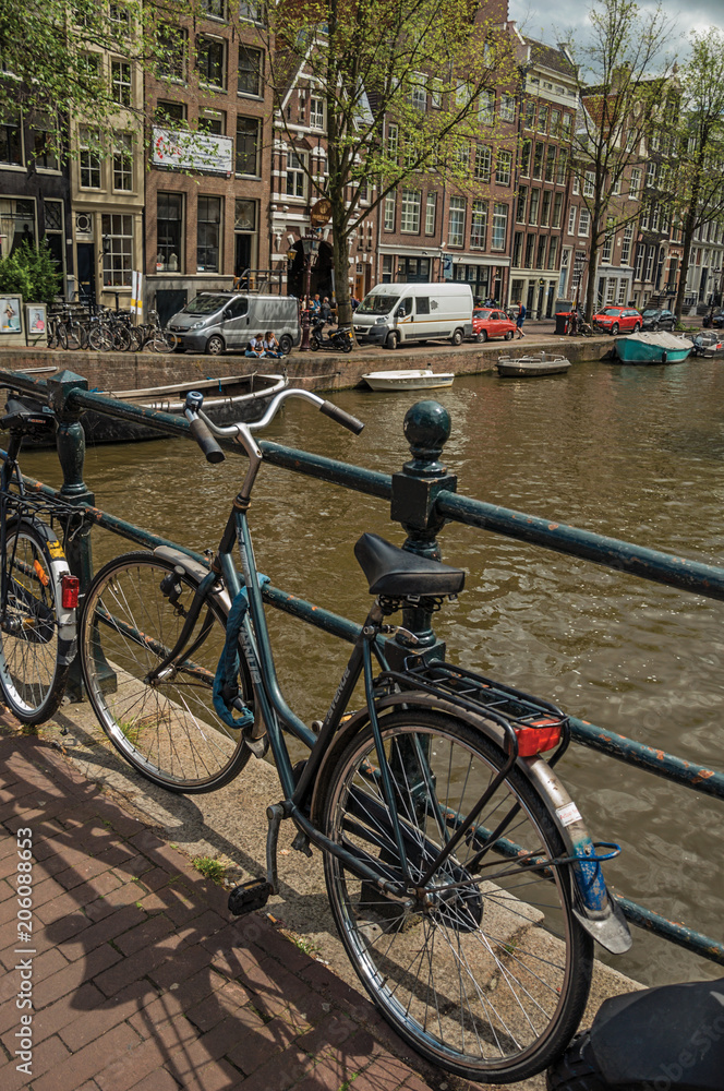 Bridge on canal with iron balustrade, bicycles, old buildings and boats in Amsterdam. Famous for its huge cultural activity and full of graceful canals. Northern Netherlands.