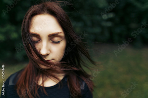 stylish beautiful woman calm portrait with windy hair posing on background green trees in summer park, space for text
