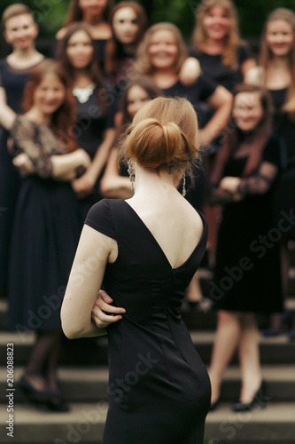 luxury gorgeous woman back in black dress standing in front of group of ladys on background of stairs in city © sonyachny