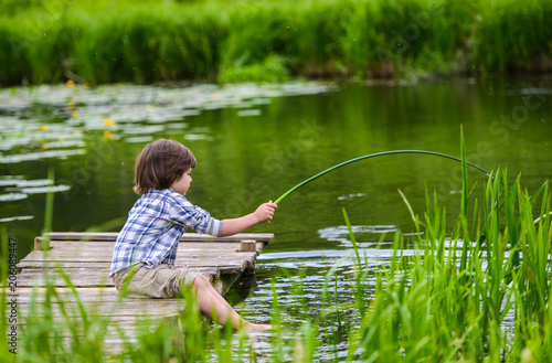 the boy sits on a wooden bridge with his feet in the water. With the plant in the hands
