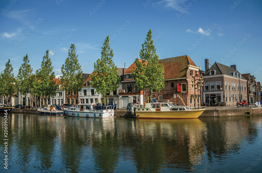Wide canal with brick houses, boats moored on its bank reflected in water and blue sky of sunset in Weesp. Quiet and pleasant village full of canals and green near Amsterdam. Northern Netherlands.