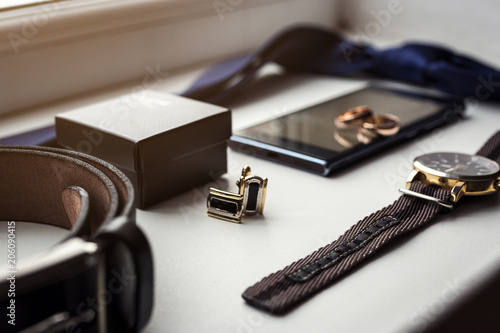 Different men's accessories such as: cufflinks, watches, rings, belt, tie and phone - are on the table