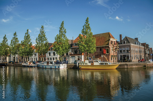 Wide canal with brick houses, boats moored on its bank reflected in water and blue sky of sunset in Weesp. Quiet and pleasant village full of canals and green near Amsterdam. Northern Netherlands. © Celli07