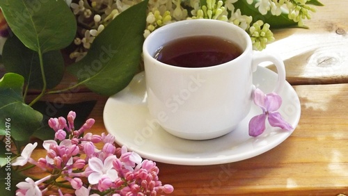 A Cup of tea on a wooden table and a bouquet of lilacs.