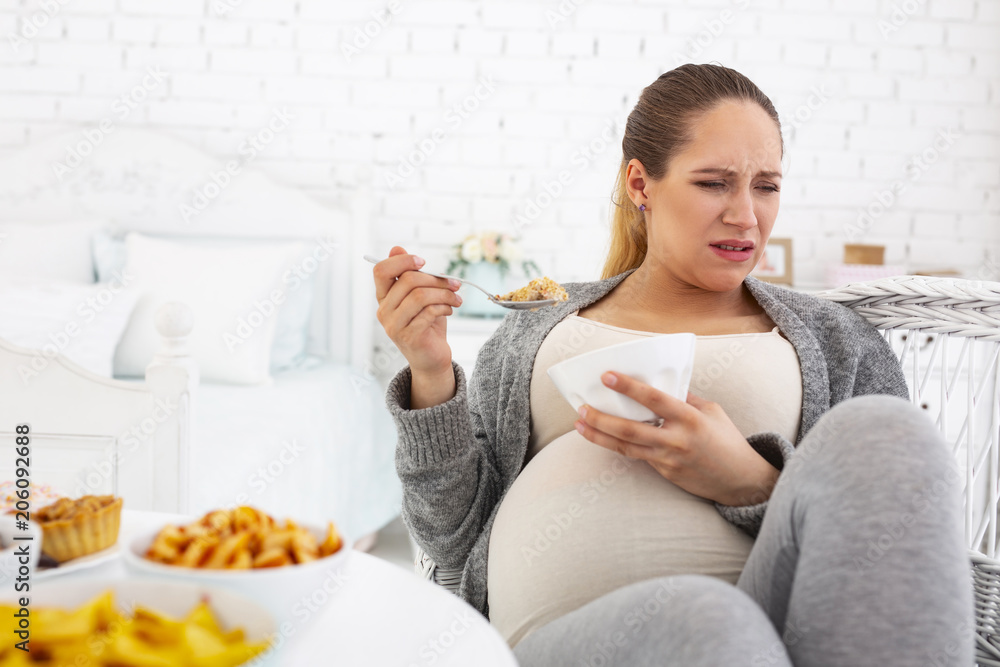 Bowl with granola. Upset pregnant woman sitting while consuming granola