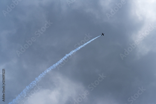 A jet plane flies from left to right, behind it is a tail of smoke photo